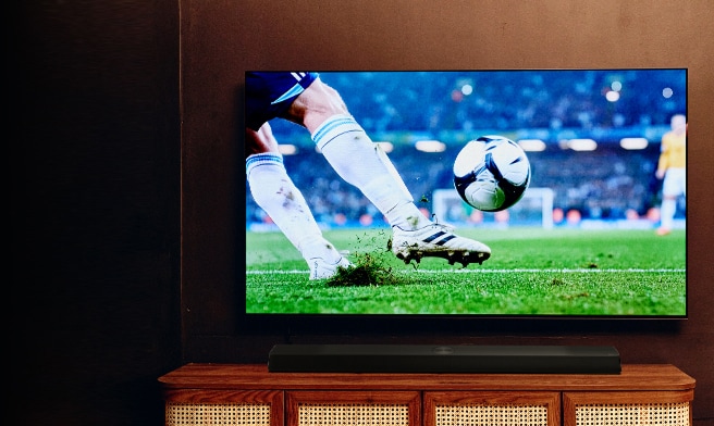 Gran televisor mostrando un partido de fútbol sobre un mueble de TV de madera en una acogedora sala de estar.