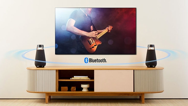 Imagen de dos altavoces XO3 colocados en el estante del TV. Se conectan al TV por Bluetooth y muestran la onda sonora por todo el salón