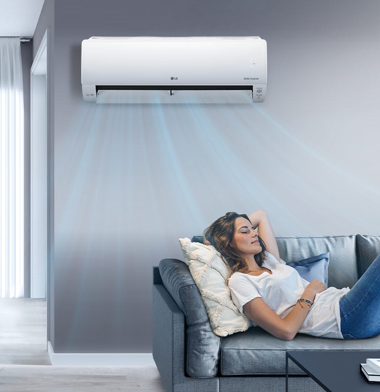 A woman lounges on a couch in a living room with the LG air conditioner installed above her on the wall. Blue streams of air are on the image to indicate it is on and cooling the room.