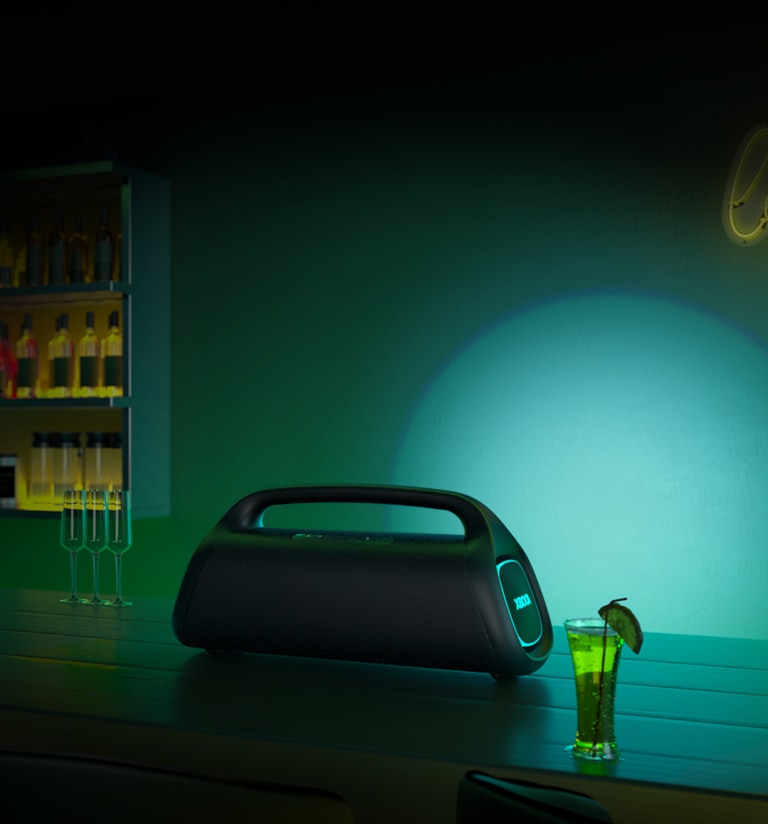 LG XBOOM Go XG9 está colocado sobre una mesa de bar. Proyecta una iluminación de escenario verde y azul.