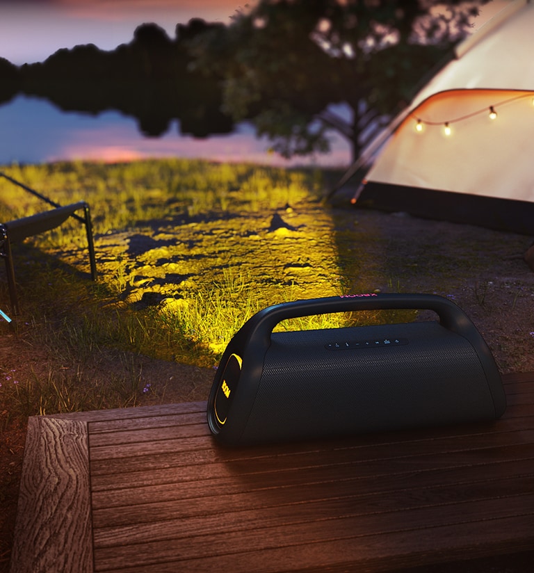 LG XBOOM Go está colocado sobre un suelo de madera proyectando una luz de escenario en un camping.