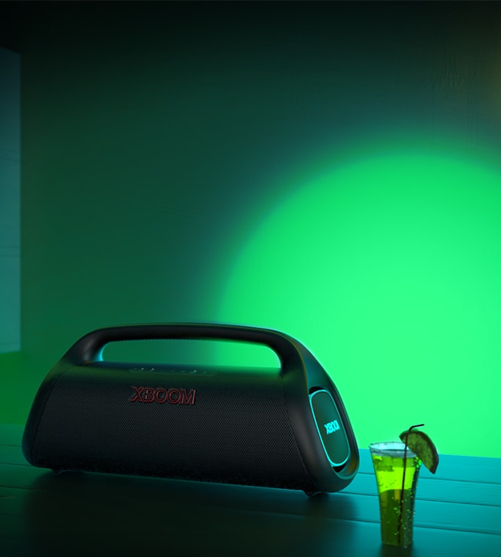 LG XBOOM Go XG9 está colocado sobre una mesa de bar. Proyecta una iluminación de escenario verde y azul.