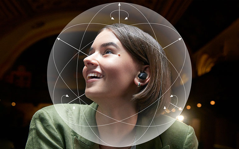 Una mujer con T90S sonríe. Se muestra una esfera ilustrativa alrededor de su cabeza para enfatizar la función de seguimiento™ Dolby Head.