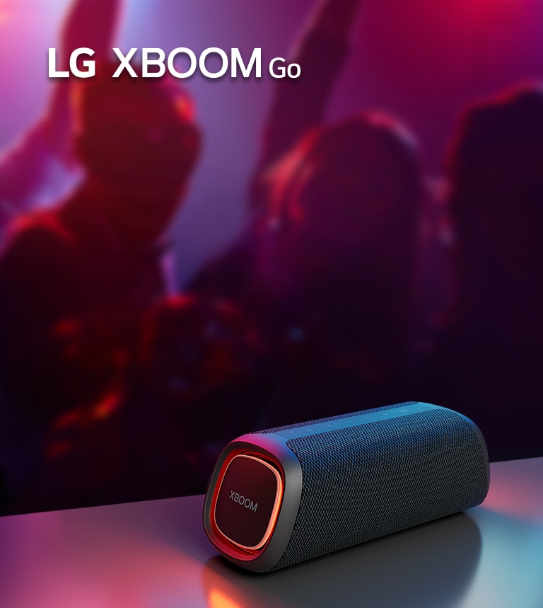 Imagen del altavoz LG XBOOM Go XG5 sobre una mesa de metal con las luces LED encendida en naranja. Detrás de la mesa, se ve a gente bailando.