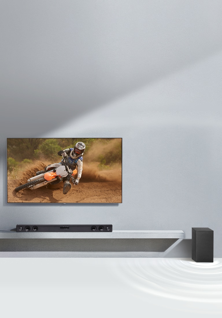 La barra de sonido LG SQC2 y el televisor LG están colocados juntos en el salón. El subwoofer está colocado junto a la barra de sonido. El televisor está encendido y muestra una imagen de una motocicleta.