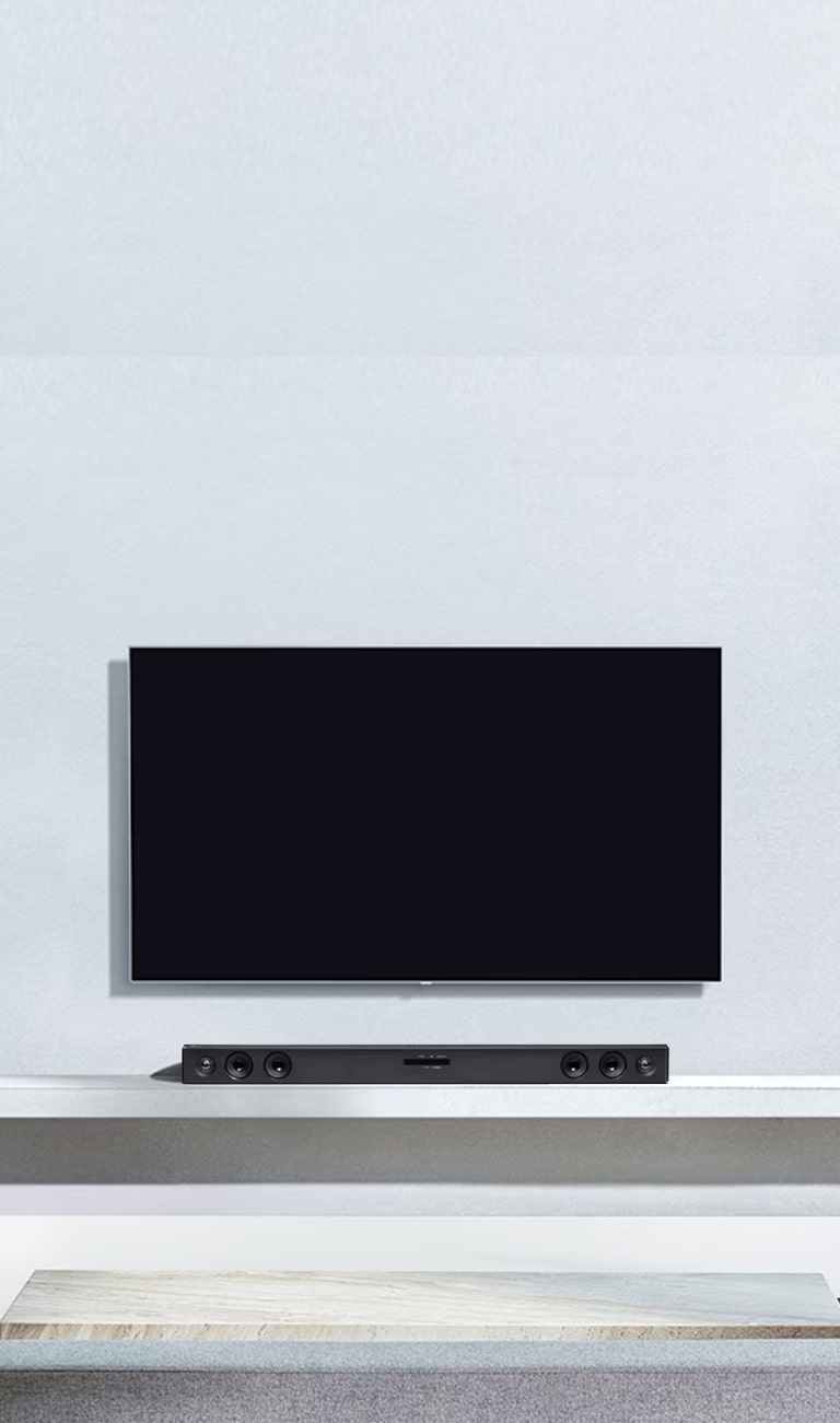 El televisor LG está colgado en la pared gris. Y la barra de sonido LG SQC2 está colocada en la estantería del salón. Y el subwoofer está colocado junto a la estantería. La imagen ilustra que la barra de sonido hace juego con el televisor LG y complementa la estancia.