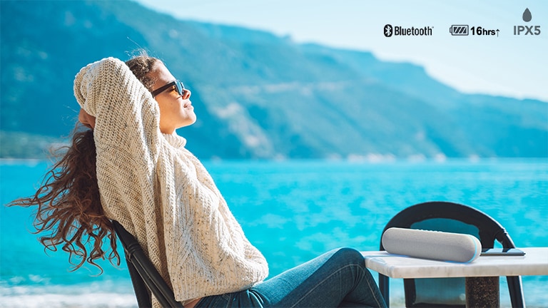 Una mujer disfrutando de la música en la terraza al aire libre con el altavoz LG XT7S.