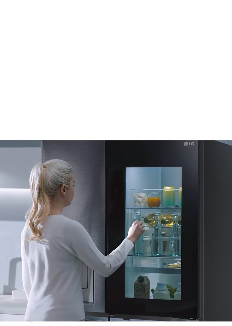 Mujer rubia abre la puerta de un frigorífico LG, mostrando bebidas y alimentos en una cocina moderna.