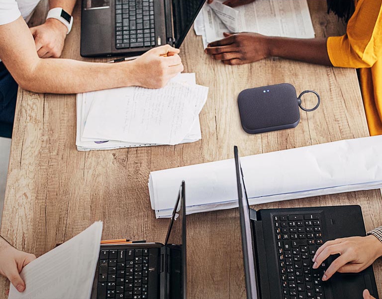 4 personas están trabajando en un escritorio, cada uno con su propia computadora portátil. Los rostros no se muestran, algunos están escribiendo, algunos están escribiendo. El altavoz XBOOM Go PN1 se coloca sobre un escritorio.