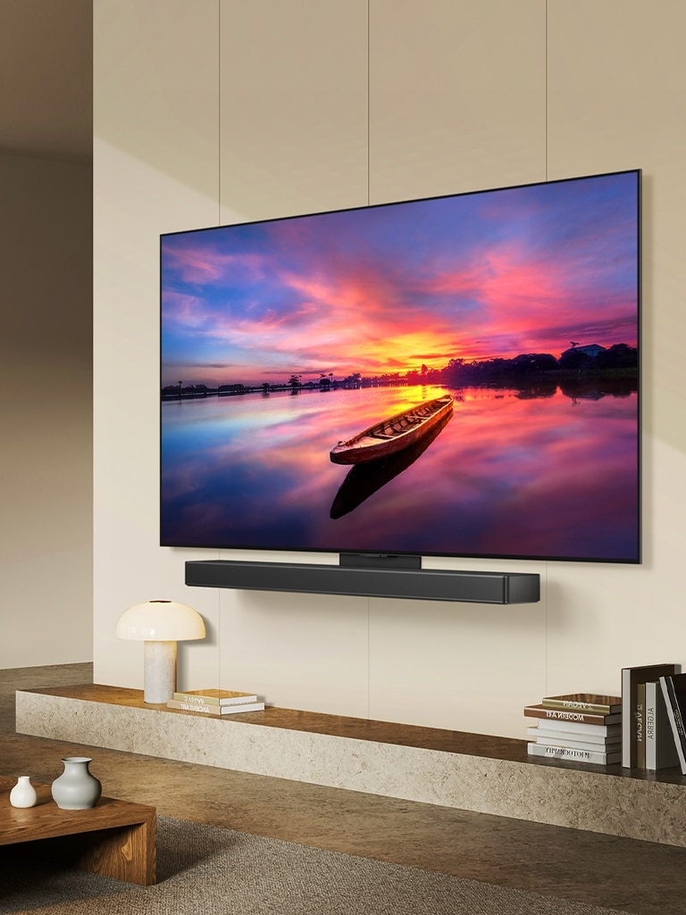 Televisor LG OLED, OLED C4, orientado 45 grados a la izquierda mostrando una hermosa puesta de sol con un barco en un lago, mientras el televisor está conectado a una LG Soundbar mediante el soporte Synergy en un salón minimalista.