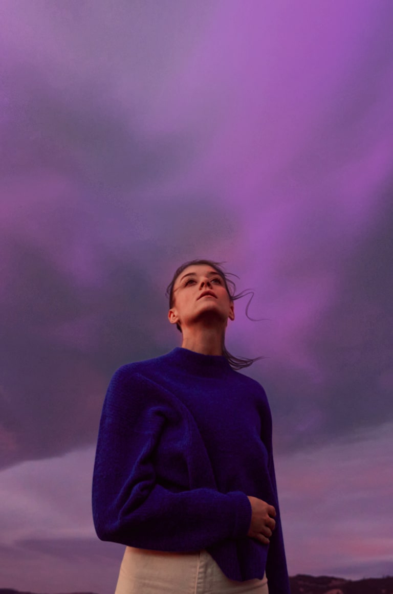 Una mujer está mirando un cielo de color púrpura. Su pelo se mueve ligeramente por el viento.