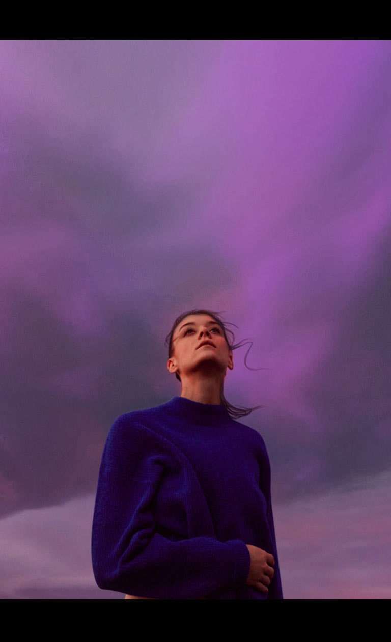 Una mujer está mirando un cielo de color púrpura. Su pelo se mueve ligeramente por el viento