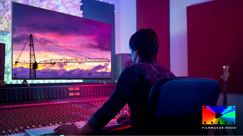 Un director de cine está mirando un gran monitor de TV, editando algo. La pantalla de TV muestra una grúa torre en el cielo púrpura. El logotipo de Modo FILMMAKER aparece en la esquina inferior derecha.