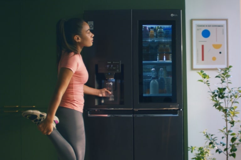 Una mujer cogiendo agua del dispensador del frigorífico después de haber hecho ejercicio.