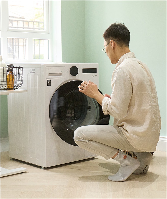 Hombre cargando ropa en una lavadora.