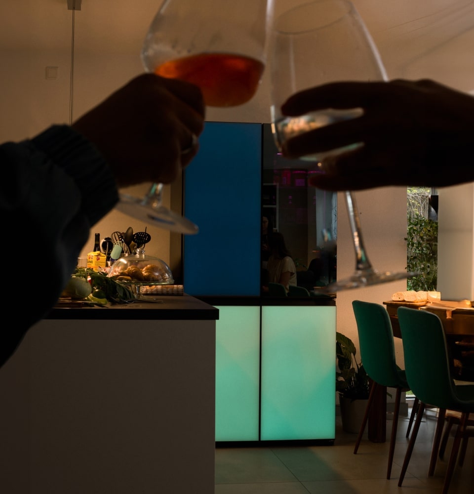 Dos manos chocan copas frente al LG MoodUP Refrigerator, que presenta paneles de colores vibrantes perfectos para el ambiente de la fiesta.