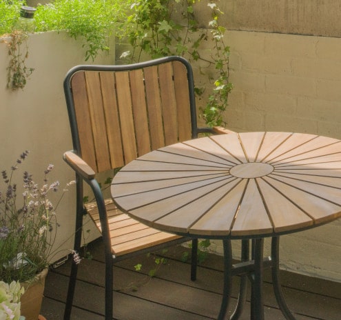 Una mesa de patio de madera con una silla a juego rodeada de plantas.