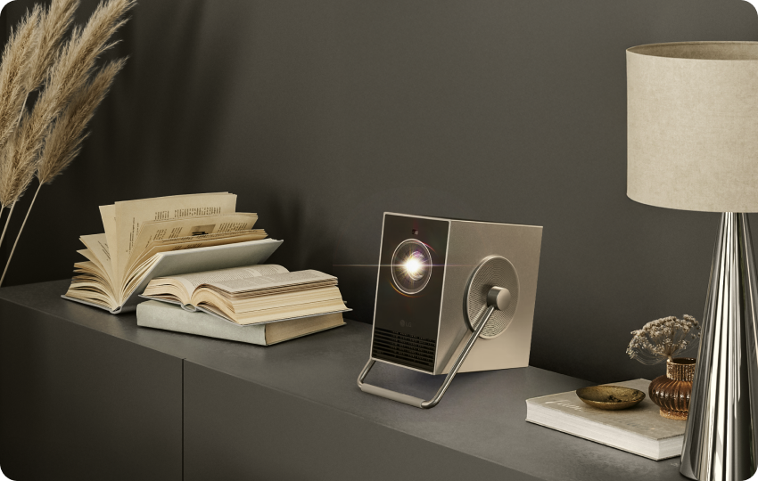 El proyector LG CineBeam Q colocado en un estante con libros y decoración en un espacio de vida elegante.