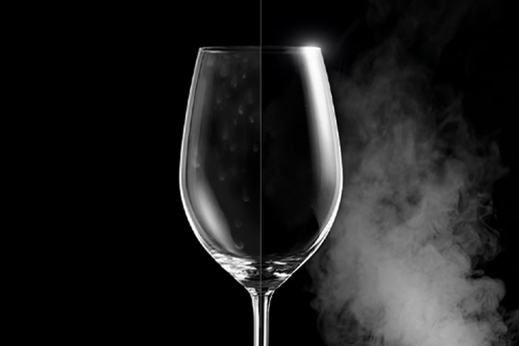 Una copa de vino con manchas de agua en un lado y cristalina en el otro, mostrando la diferencia después del lavado a vapor.