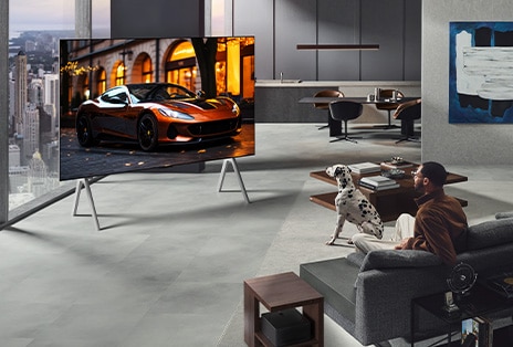 Salón con un televisor True Wireless de LG y una LG Soundbar montada en la pared. La Zero Connect Box apenas se ve debajo de una mesa auxiliar junto al sofá, lo que demuestra lo fácil que es colocarla en cualquier lugar. La disposición del salón está visualmente ordenada y despejada.