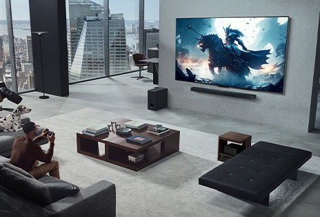 Sala de estar con una persona jugando a un videojuego en su televisor True Wireless de LG montado en la pared y LG Soundbar. Sostiene en la mano un mando a distancia, pero la consola de juego no se ve de manera inmediata. Tampoco se ven cables. La Zero Connect Box está perfectamente guardada y apenas se ve bajo una mesa auxiliar.