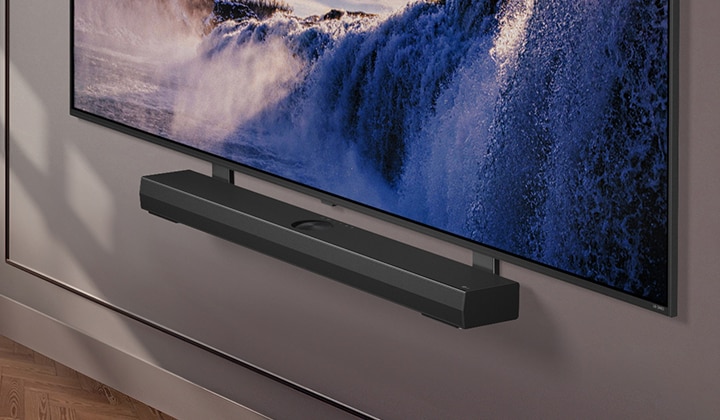 El soporte Synergy se muestra con un televisor LG QNED. El soporte sinérgico y el televisor LG QNED TV se unen mientras se desplaza hacia abajo para mostrar la parte inferior del televisor. Aparece la barra de sonido LG colocada en el Synergy Bracket. El fondo es la pared.