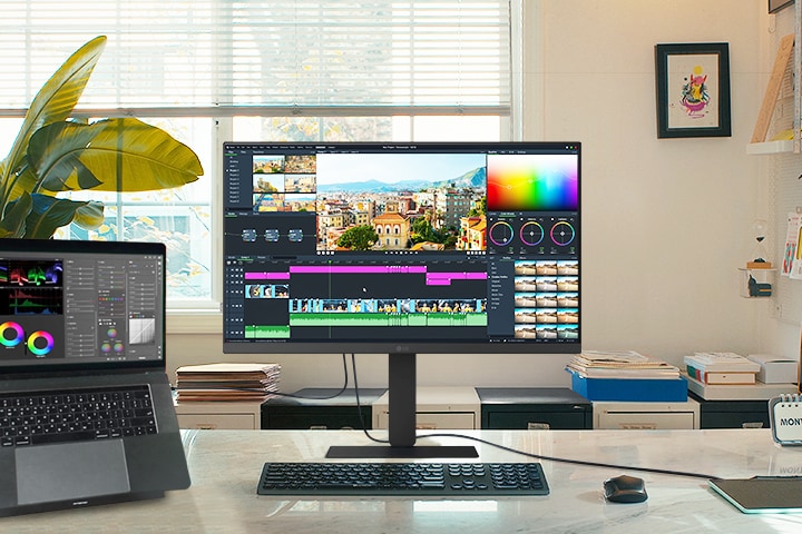 Un espacio de trabajo creativo con un monitor LG y un portátil conectado, ambos con una interfaz de edición de vídeo con herramientas de gradación de color y una línea de tiempo.