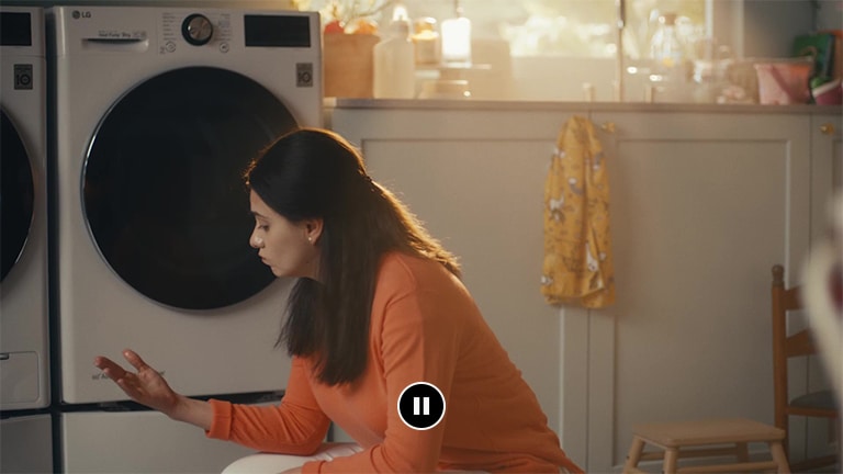 Una mujer está sentada delante de la lavadora mirando sus manos mojadas