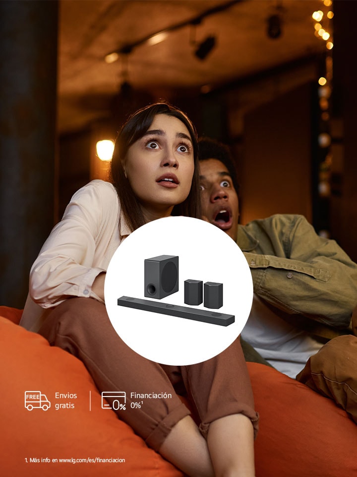 Vista aérea de LG Soundbar con altavoces traseros y subwoofer colocada en una estantería de madera marrón de una habitación negra y oscura donde la única luz que ilumina el sistema de sonido.