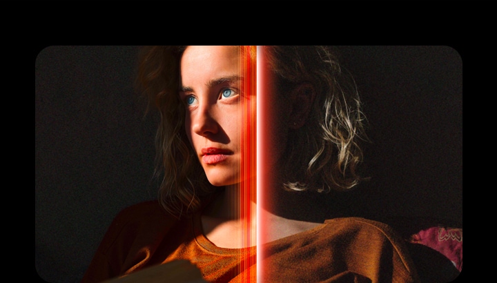 Une femme aux yeux bleus perçants et avec un haut orange sur un fond sombre. Des lignes rouges représentant les améliorations apportées par l’IA couvrent une partie de son visage, éclatent et détaillé, tandis que le reste de l’image semble terne.