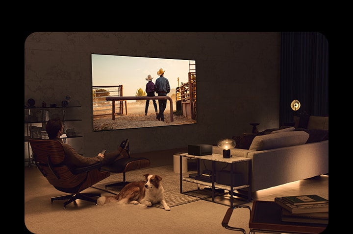 Un homme regarde un film de cow-boy avec son chien dans un espace de vie confortable en soirée. Aucun câble n'entoure le téléviseur OLED LG fixé au mur, et le boîtier de connexion sans fil est posé sur une table d'appoint. Ensuite, l'image glisse vers une autre image qui montre un homme regardant un film de cow-boy avec le téléviseur LG OLED sur pied.  LG OLED TV sur un support au sol dans un espace de vie agréable et sombre. Aucun câble n'entoure le téléviseur LG OLED et son support, et le boîtier de connexion sans fil est posé sur une table d'appoint.