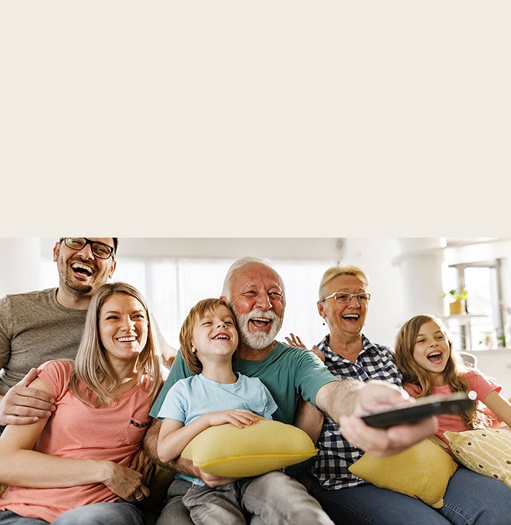 Une famille est assise et rit, tandis que le grand-père dirige la télécommande vers l’extérieur.