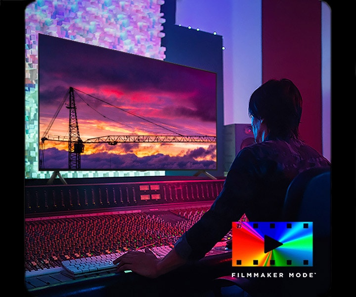 Un homme dans un studio d’édition obscur qui regarde un téléviseur LG affichant un coucher de soleil. En bas à droite de l’image, on voit un logo FILMMAKER Mode.