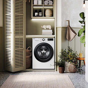 Lave-linge LG F94R35WHS blanc installé dans une buanderie confortable avec des placards à persiennes et des plantes vertes.