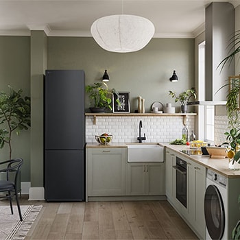 Réfrigérateur-congélateur LG GBV22NCCEP Noir Mat (203 cm de haut), intégré élégamment dans une cuisine moderne vert olive avec parquet et plantes d'intérieur.