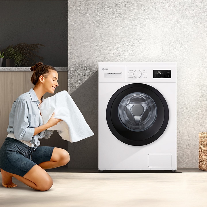 Žena klečící před pračkou v obývacím pokoji a držící čistou deku.