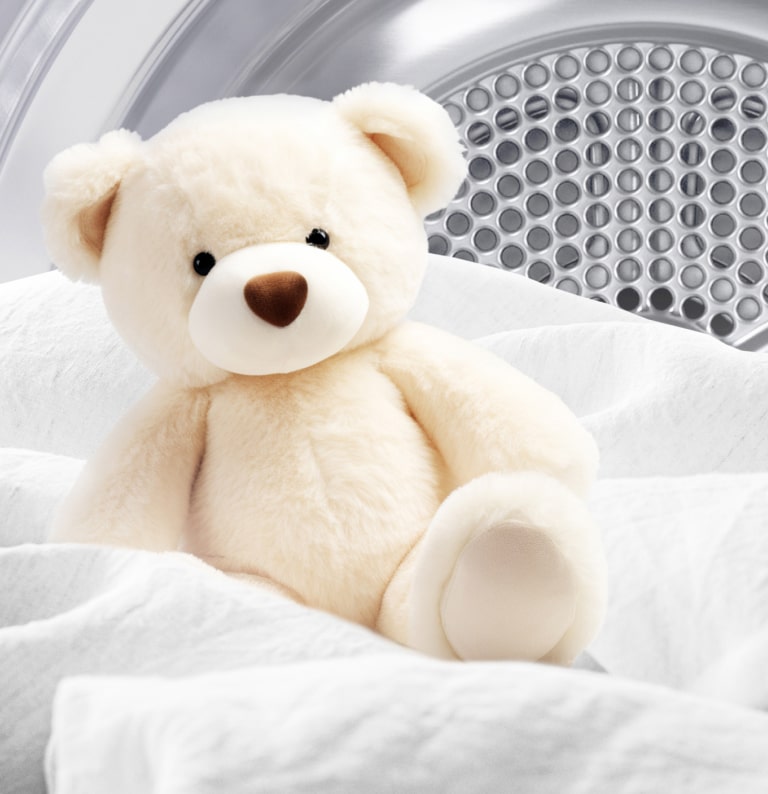 Image d’un ours en peluche propre et d’un tissu blanc dans un tambour de séchage.