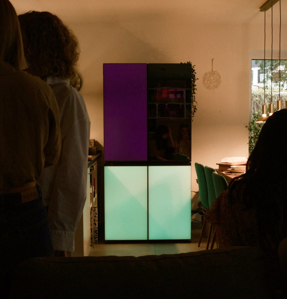 Derrière les gens se trouvent le LG MoodUP Refrigerator, qui présente des panneaux de couleurs vibrantes, parfaits pour l'ambiance de fête.