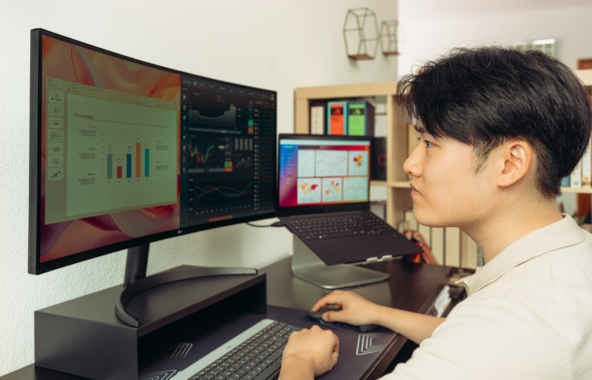 Homme travaillant à un bureau moderne avec de larges écrans et un ordinateur portable sur un support, concentré sur des graphiques et des données affichés sur les écrans.