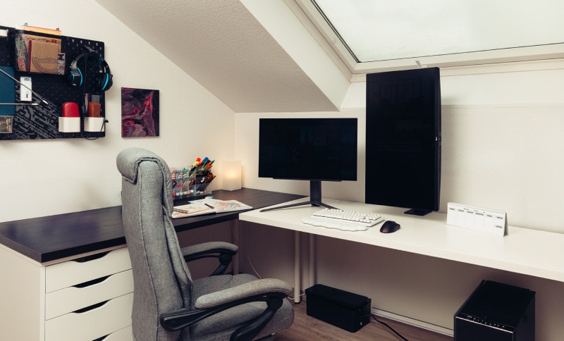 Un bureau à domicile bien rangé avec une chaise ergonomique, un bureau avec un moniteur vertical et des fournitures soigneusement disposées.