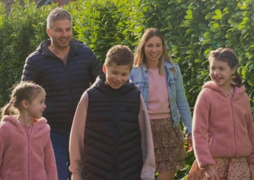 Famille de cinq personnes profitant d’une promenade en plein air, souriant et vêtue de manière décontractée, entourée de haies vertes.