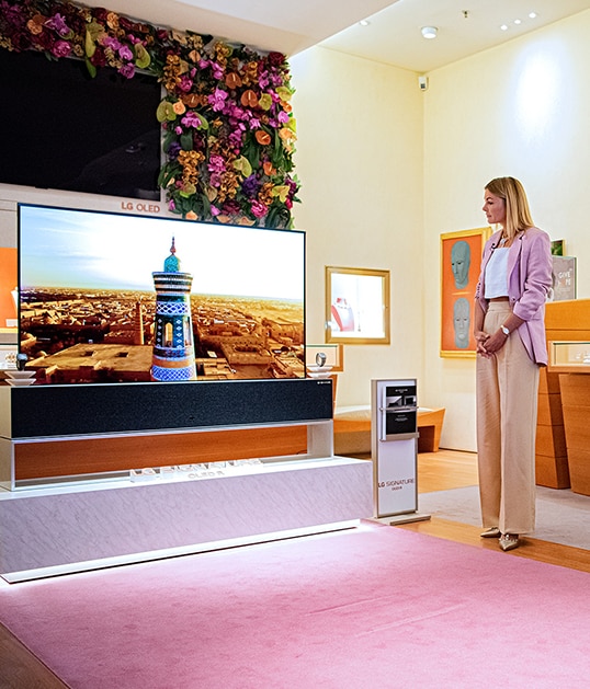 A woman observes Rollable OLED TV R as it sits in front of a wall of flowers at the LG and BVLGARI collaboration.