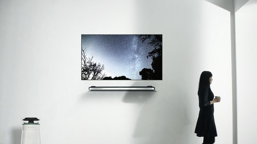 lg signature oled tv w is hung on the white wall and suki chan is standing right next to it