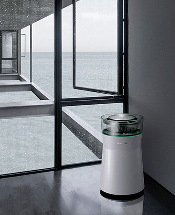 lg signature air purifier is laid on the left front side and at the back side minh tran is standing and there are many glass walls situated between air purifier and him