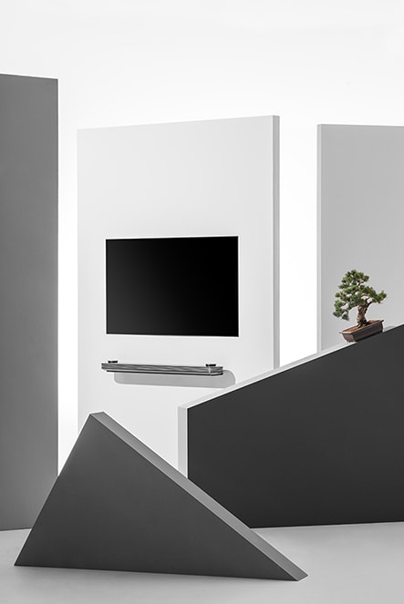 lg signature oled tv w is hung on the wall with some triangle and square sculpture and japanese plant pot around it