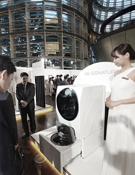 two people are looking at the lg signature washing machine and mini wash of it is being pulled out