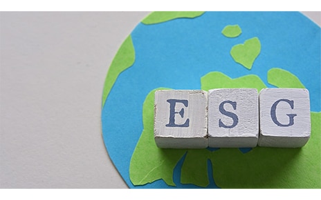 Three cubes displaying letters from the acronym ESG stand on top of a handmade picture of the world.