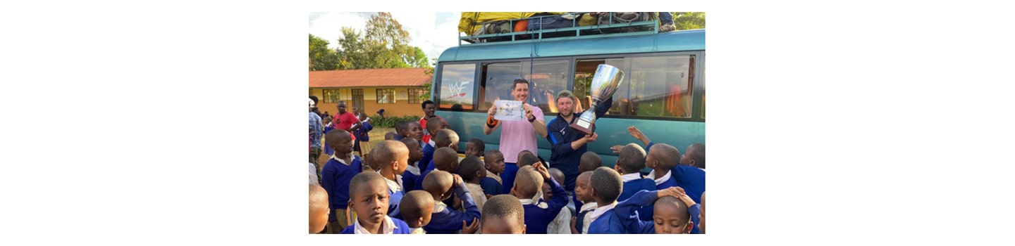 Tanzanian school children greeting two members of FC Cambounet outside their school.