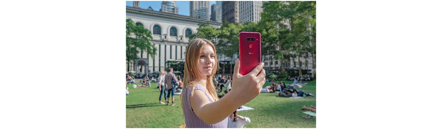 A woman holds up and looks at the display of the LG V40 ThinQ in the Carmine Red color.