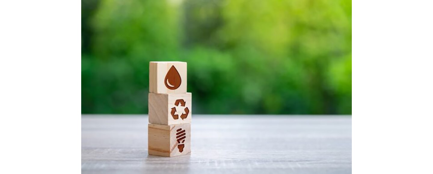 Icon representing a water droplet, a recycling logo and a light bulb are engraved on each of the three wooden cubes and placed on the table